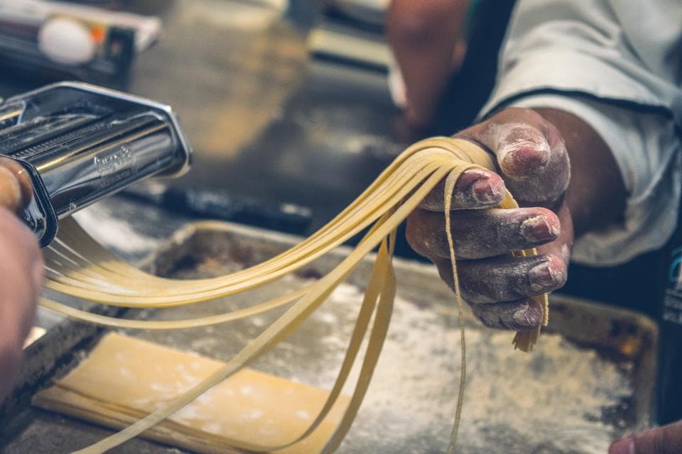 Fresh tagliatelle being cut and lifted from a pasta machine
