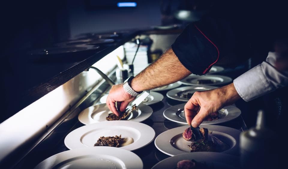 Hands plating dishes along the pass