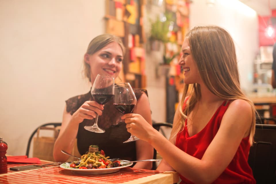Two friends raising glasses of red wine over dinner